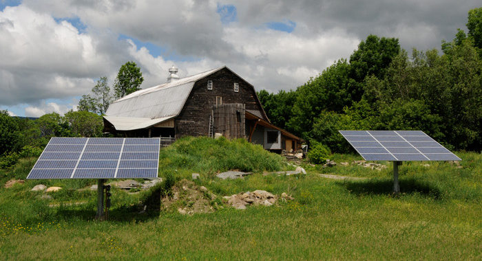 Two solar panels with a barn in the background